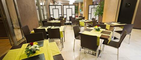 Comedor con mesas dispuestas con manteles amarillos y sillas, con un diseño moderno y una paleta de colores neutros.