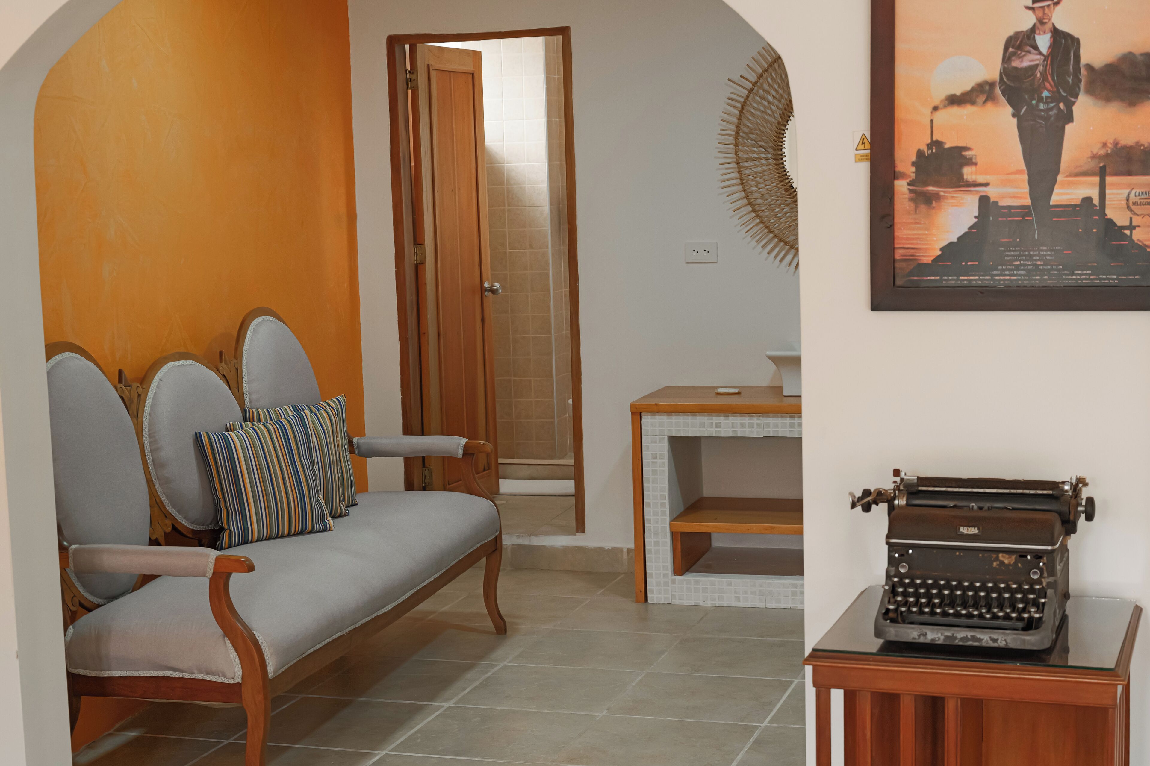 A living room with a sofa, a small table, a typewriter, and a door leading to another room.