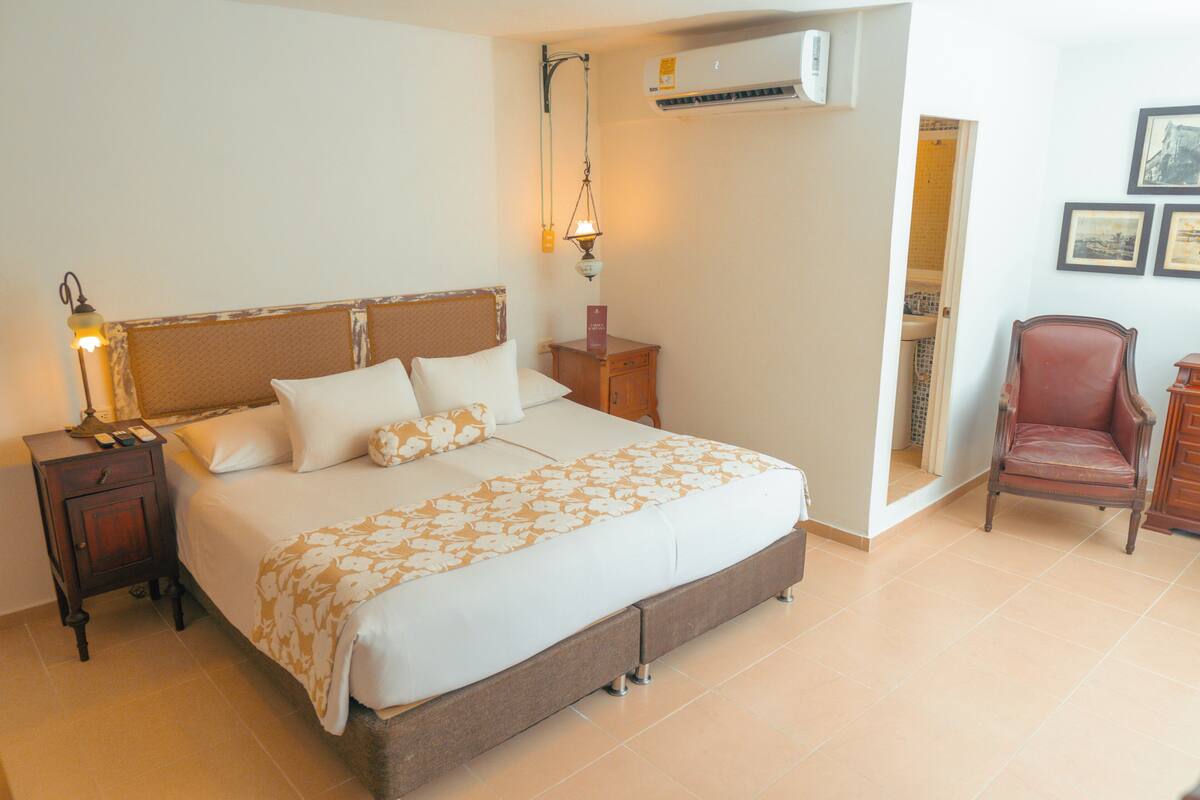 A bedroom with a bed, nightstand, lamp, and a chair.