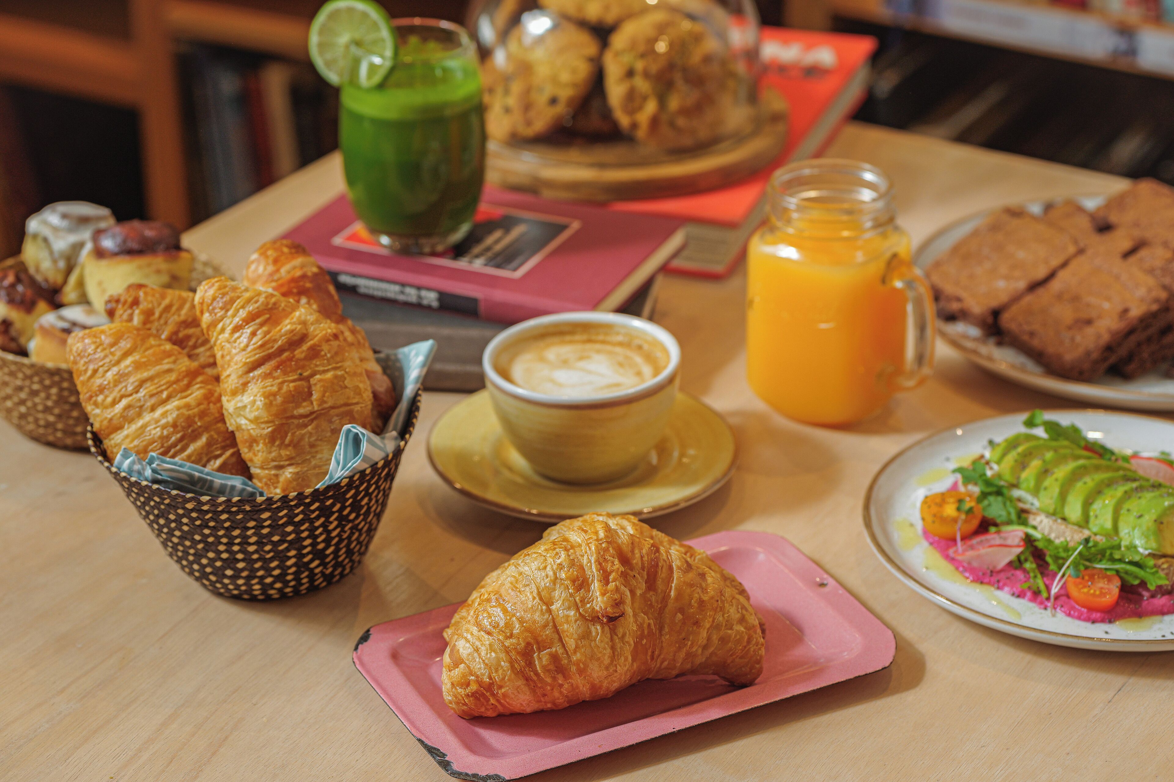 Une table de petit-déjeuner avec des croissants, une tasse de café, un verre de jus d’orange et une assiette de nourriture.