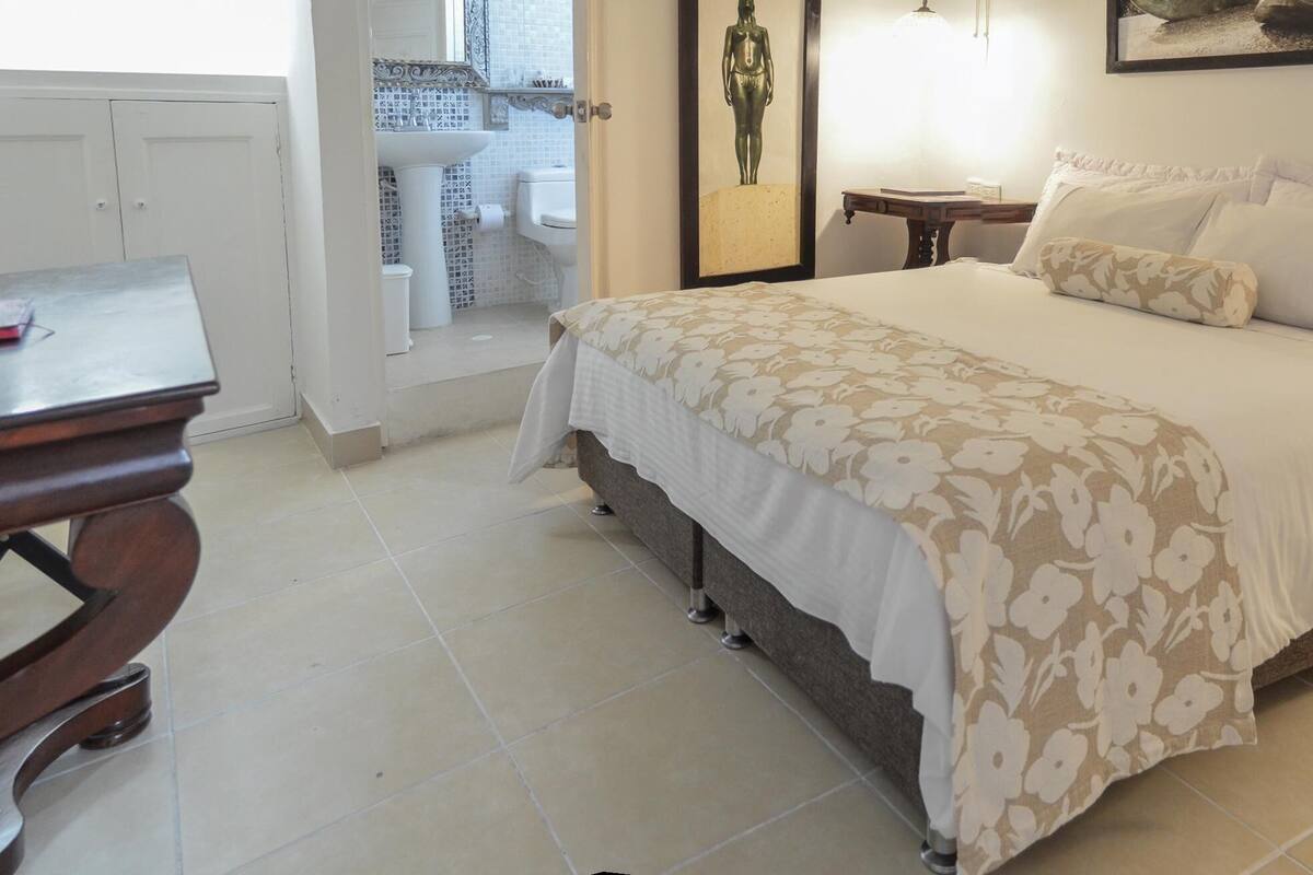 A bedroom with a bed, bedside tables, a desk, and a bathroom visible through an open door.