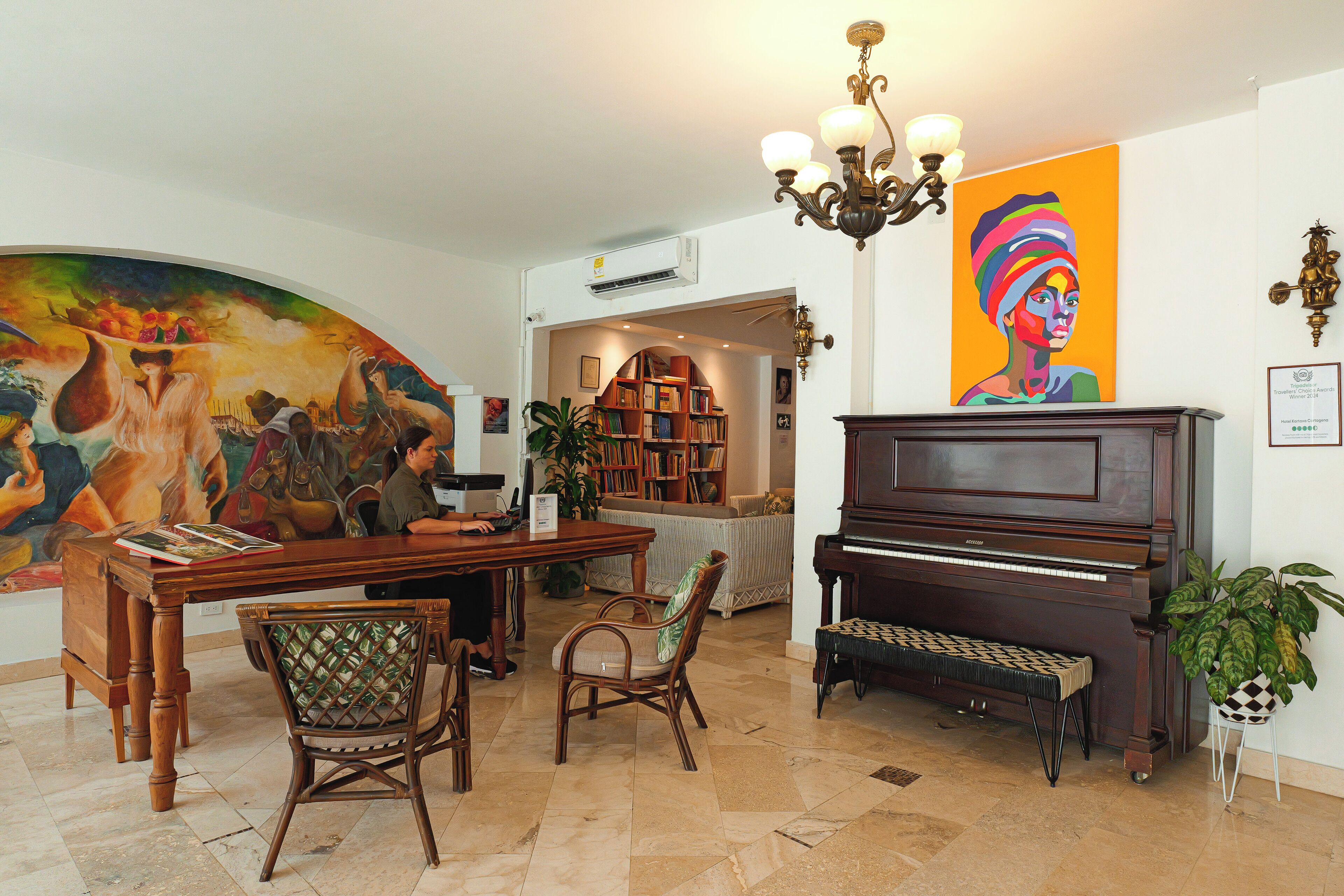 Ein Wohnzimmer mit Klavier, einem Esstisch mit Stühlen, einem Bücherregal und einem großen Gemälde an der Wand.