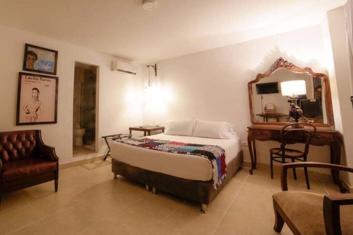 A bedroom with a bed, a wooden desk, a chair, a mirror, and a framed picture on the wall.