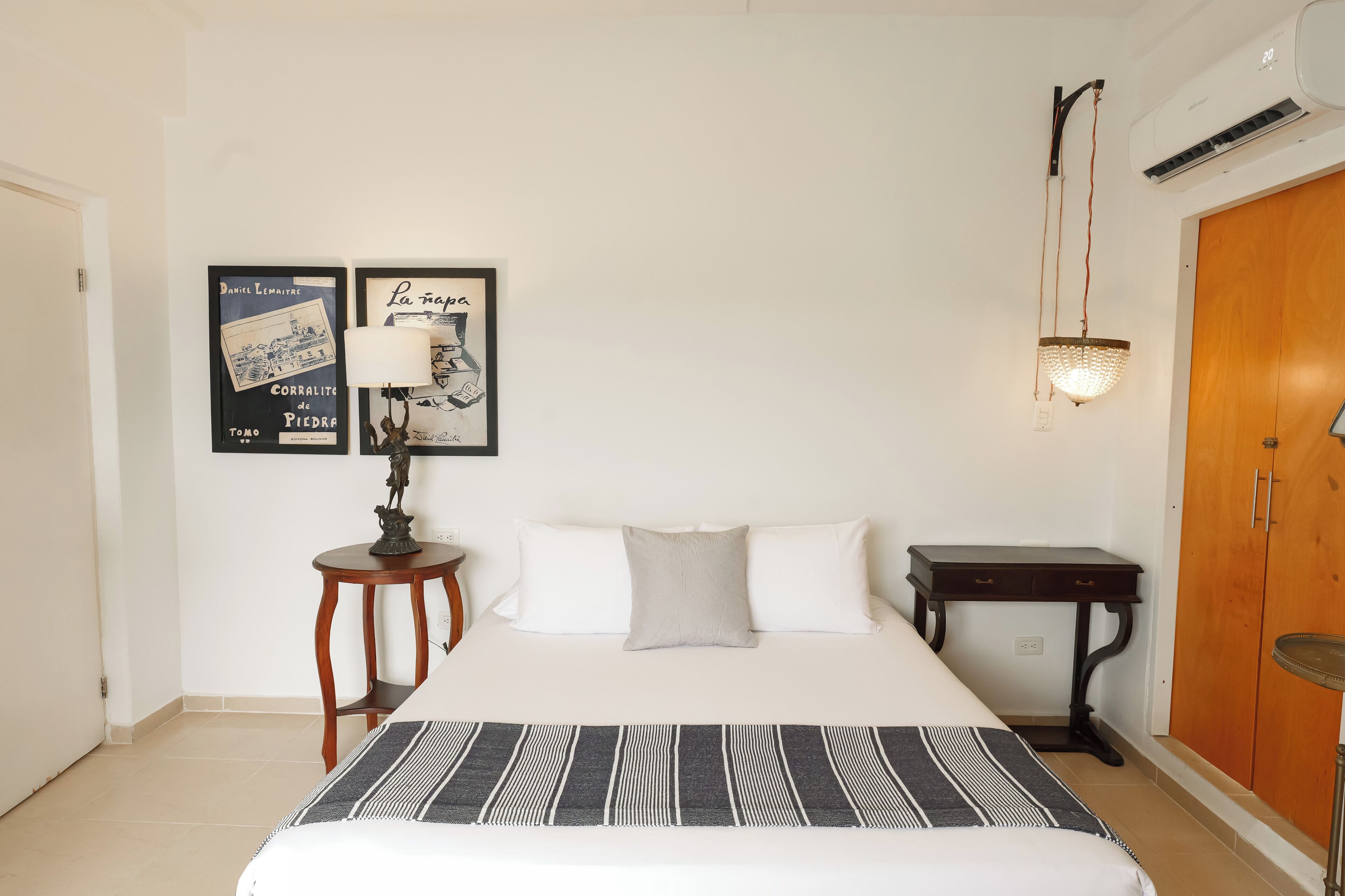 Ein Schlafzimmer mit einem Bett, einem kleinen Tisch mit Lampe, einem Kleiderschrank und zwei gerahmten Bildern an der Wand.