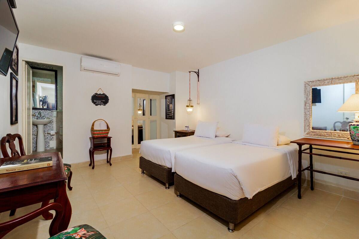 A hotel room with a bed, bedside table, chair, and a small desk with a lamp.
