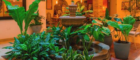 A spacious indoor area with multiple potted plants, a stone fountain, and a balcony with white railings.