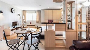 Um espaço de estar moderno e compacto, com área de refeições, cozinha compacta e um móvel de armazenamento com frente de vidro.