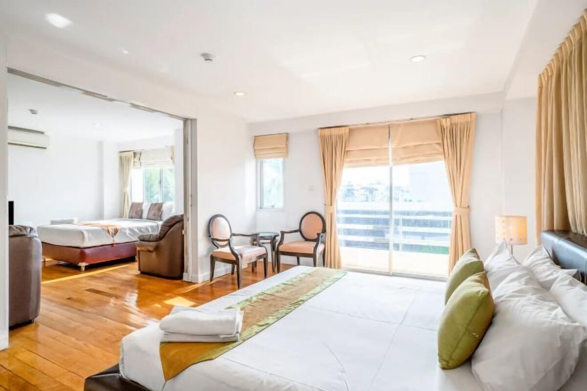 A hotel room with a large bed, a desk, and a chair. There is a window with curtains and a view of the outside.