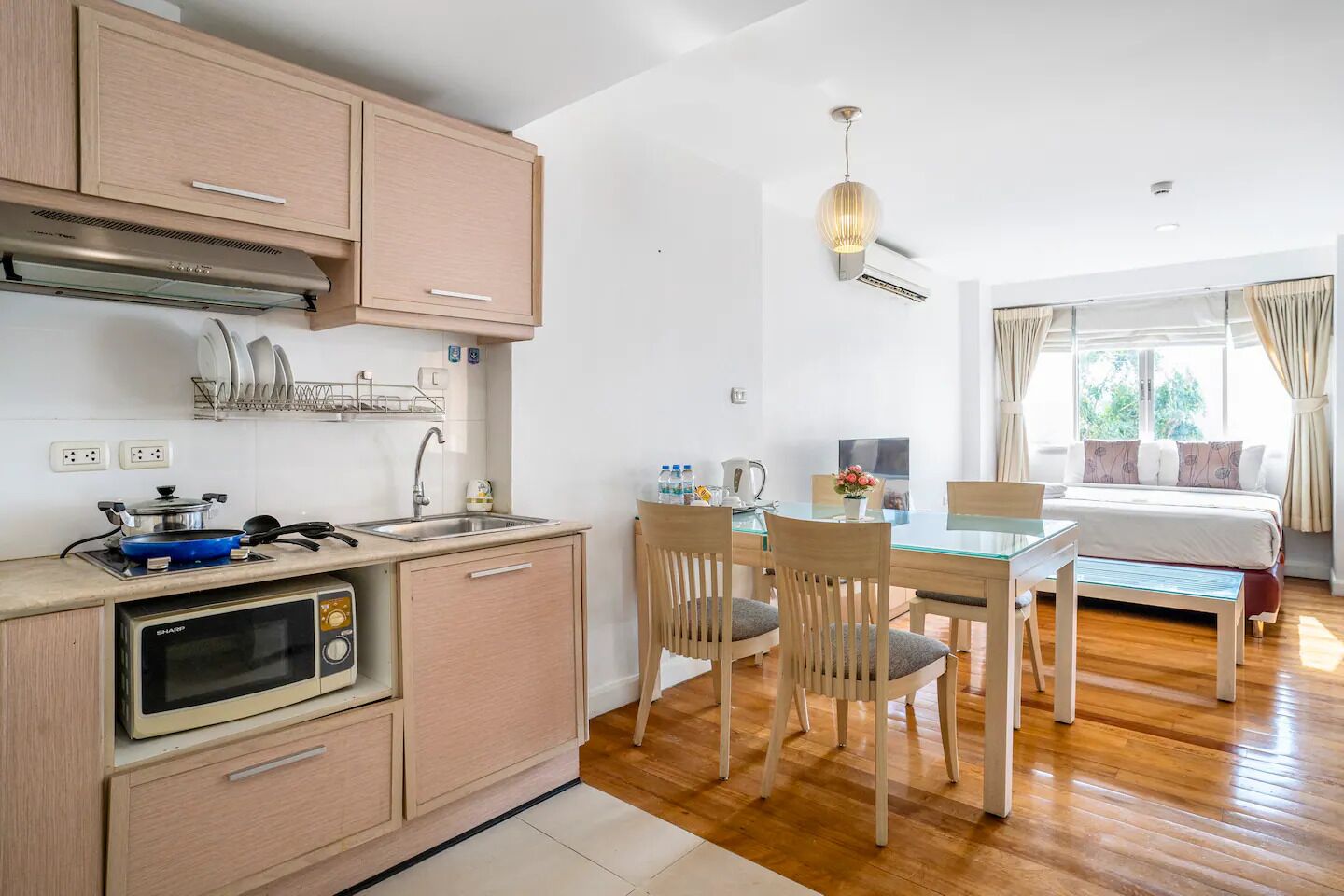 A compact kitchen with a microwave, stove, and sink. There is a dining area with a table and chairs, and a bed with a window view.