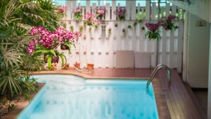 Piscina com cestos suspensos de flores e uma cerca branca ao fundo.