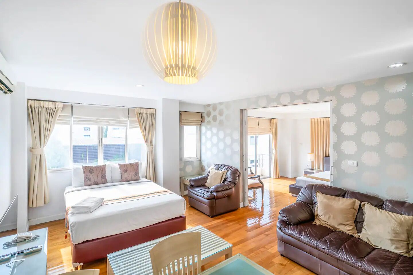A modern hotel room with a large bed, two sofas, a dining area, and a view of the outside.