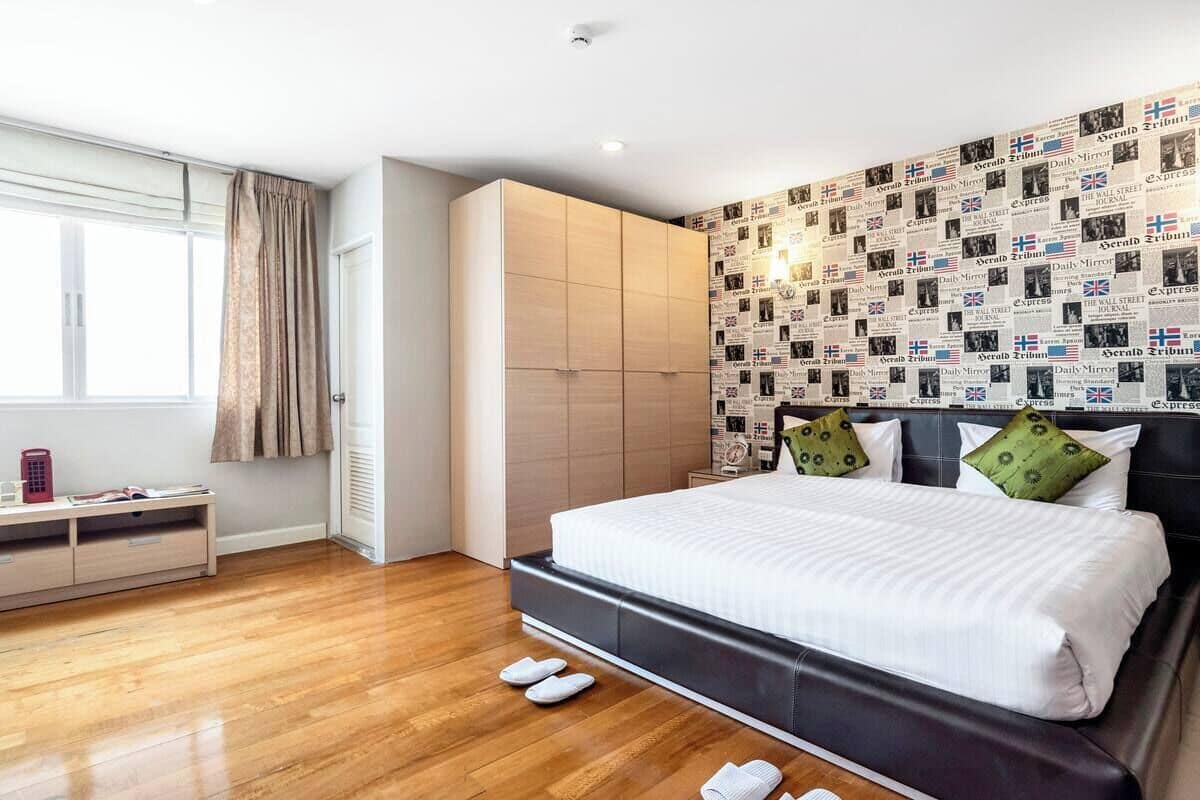 A modern hotel room with a large bed, a wardrobe, a bedside table, and a window with curtains.