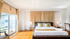 Um quarto de hotel espaçoso com uma cama grande, piso de madeira, varanda com cortinas e vista para a cidade.