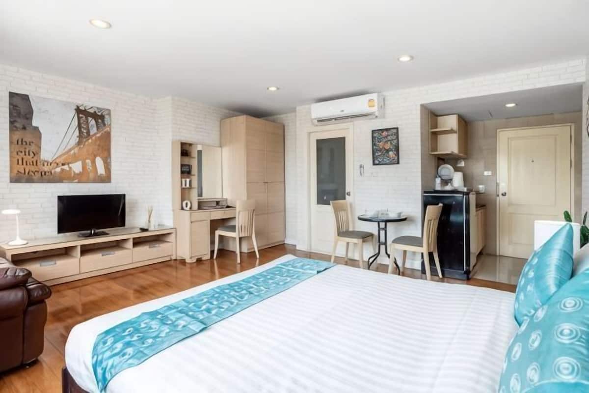 A hotel room with a bed, desk, chair, television, and a small kitchenette.