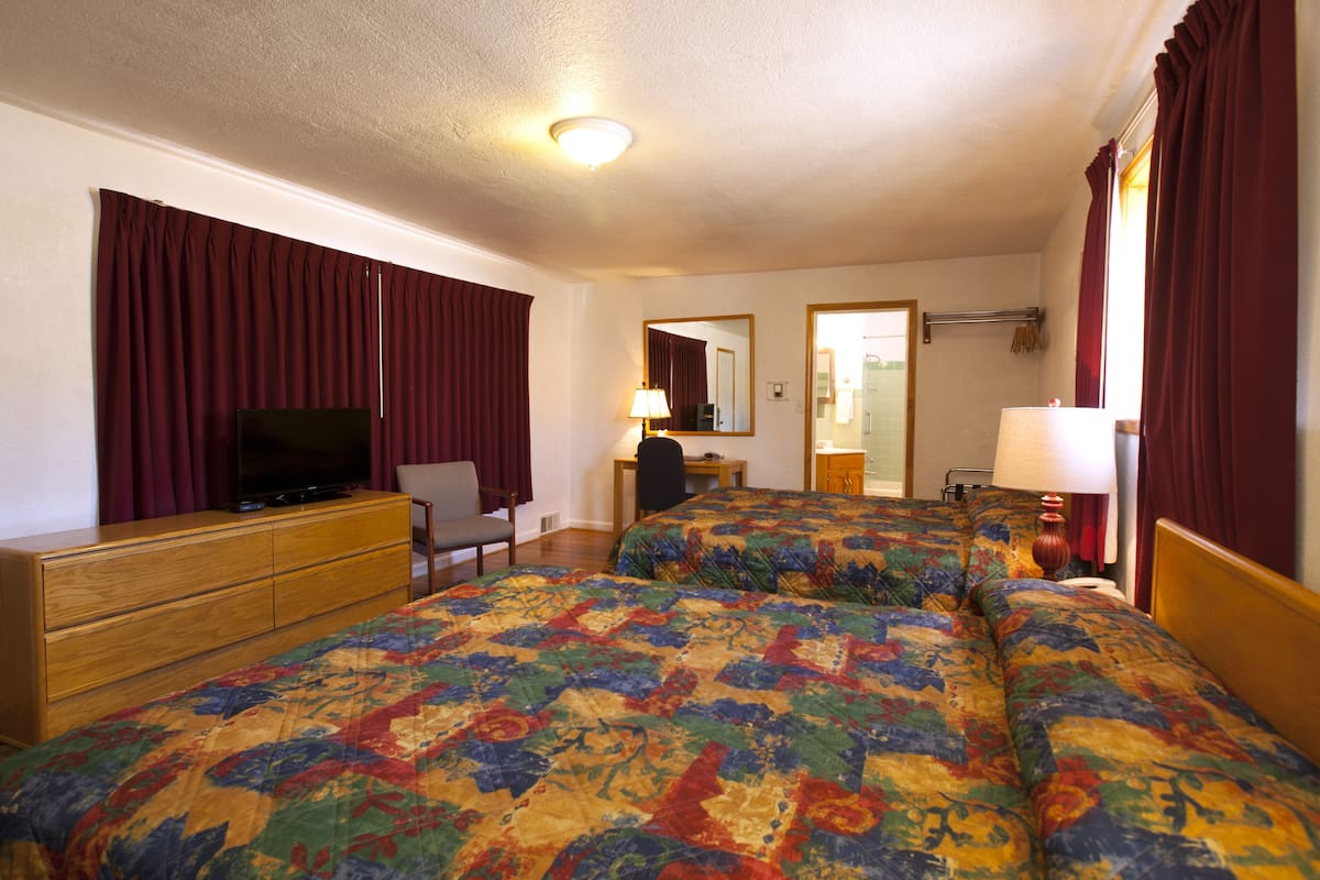 A hotel room with two beds, a TV, a desk, and a mirror.