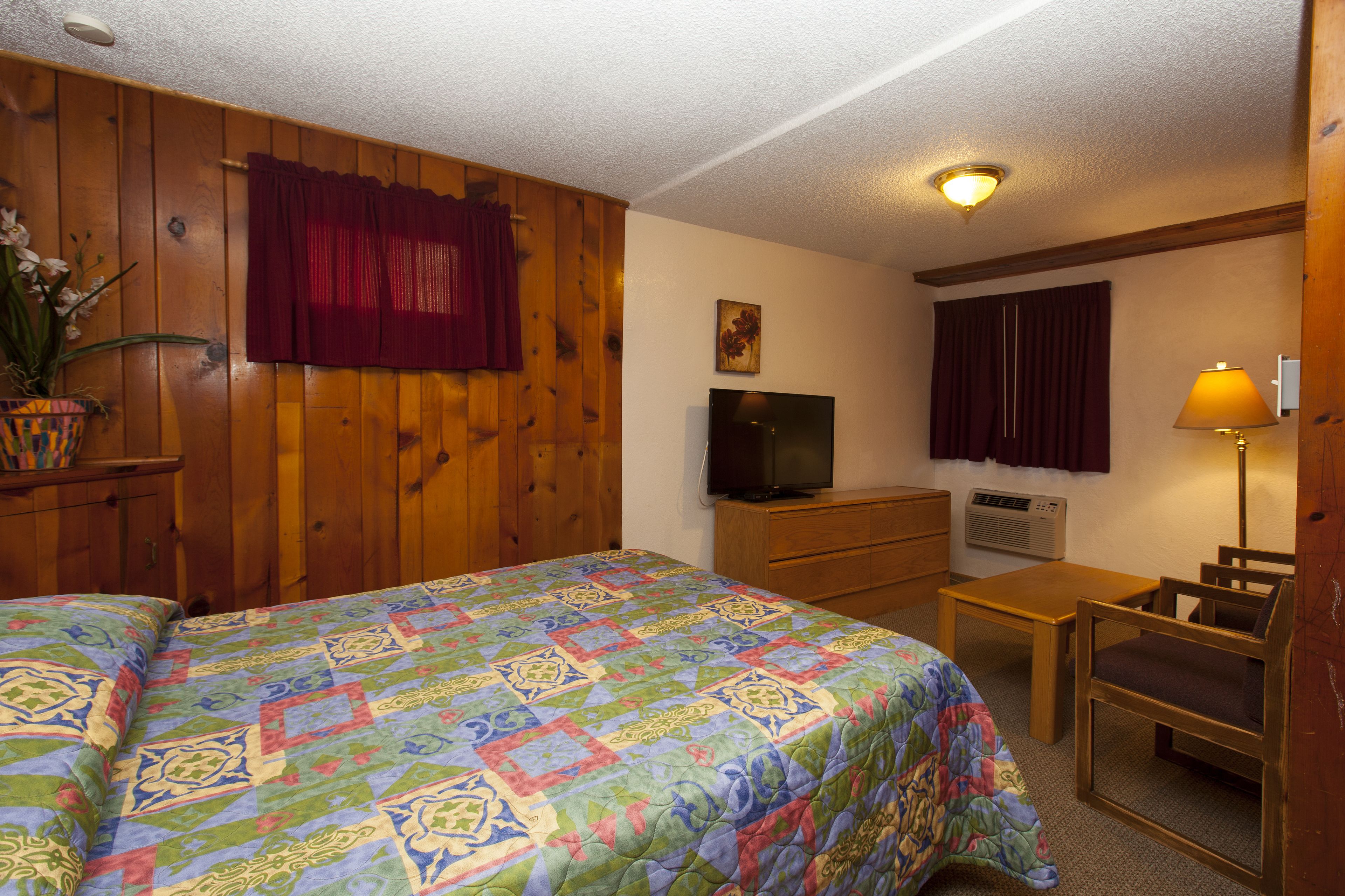 A room with a large bed, a television, a desk with a chair, and a lamp.