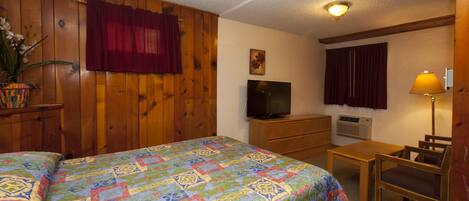 A room with a large bed, a television, a desk with a chair, and a lamp.