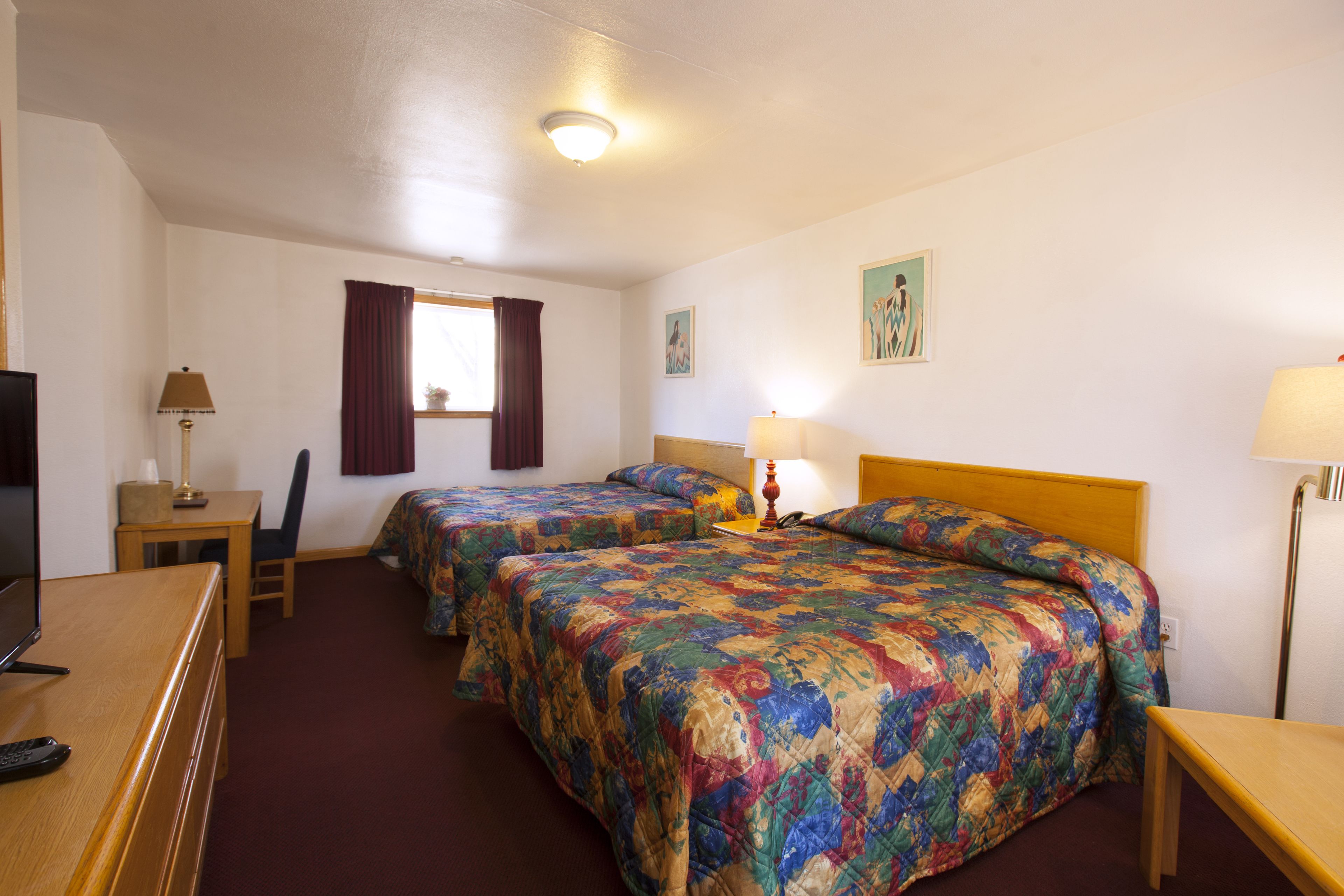 A hotel room with two beds, a desk, a TV, and a window with curtains.