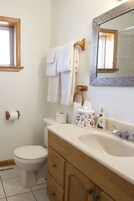 Un baño con inodoro, lavamanos y espejo. Hay toallas colgadas en un tendedero y una caja de pañuelos sobre el mueble.