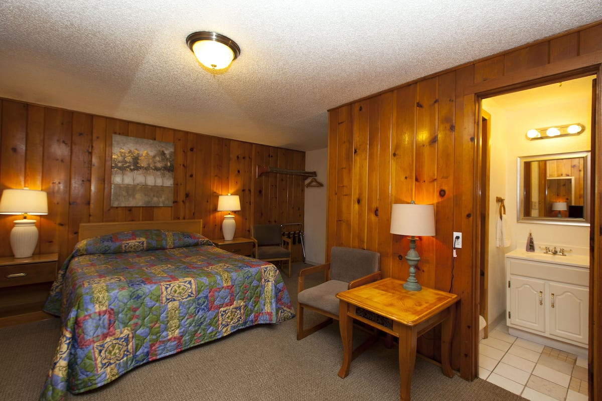 A room with a bed, a chair, a table, a mirror, and a sink.