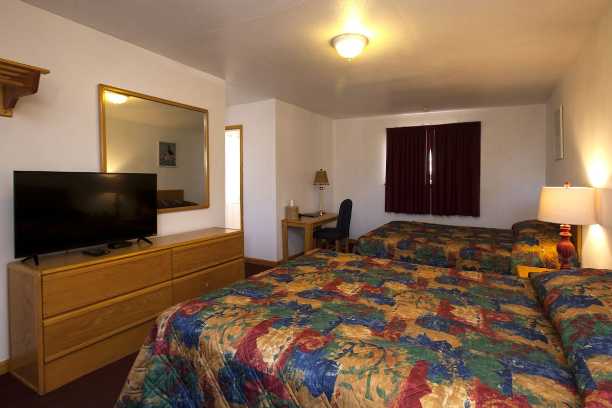 A hotel room with a large bed, a television on a wooden dresser, a desk with a chair, and a window with curtains.