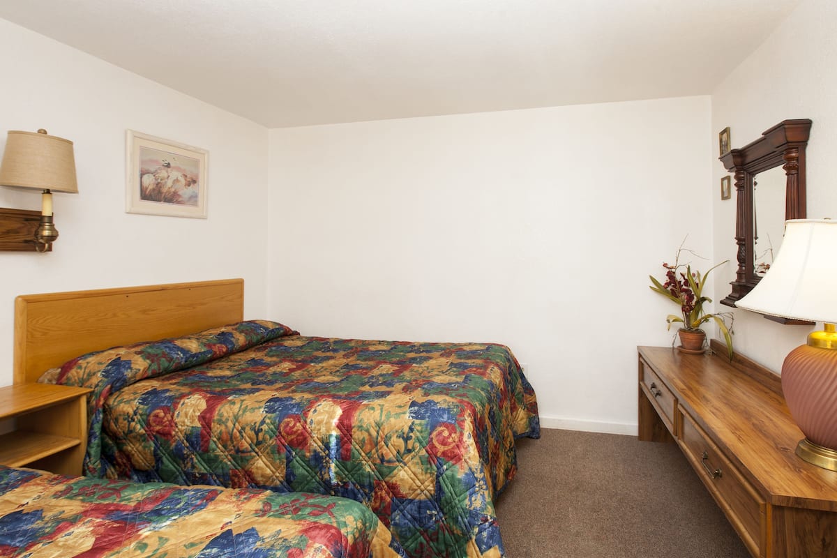 A bedroom with a wooden bed, a bedside table, a dresser, a mirror, and a lamp.