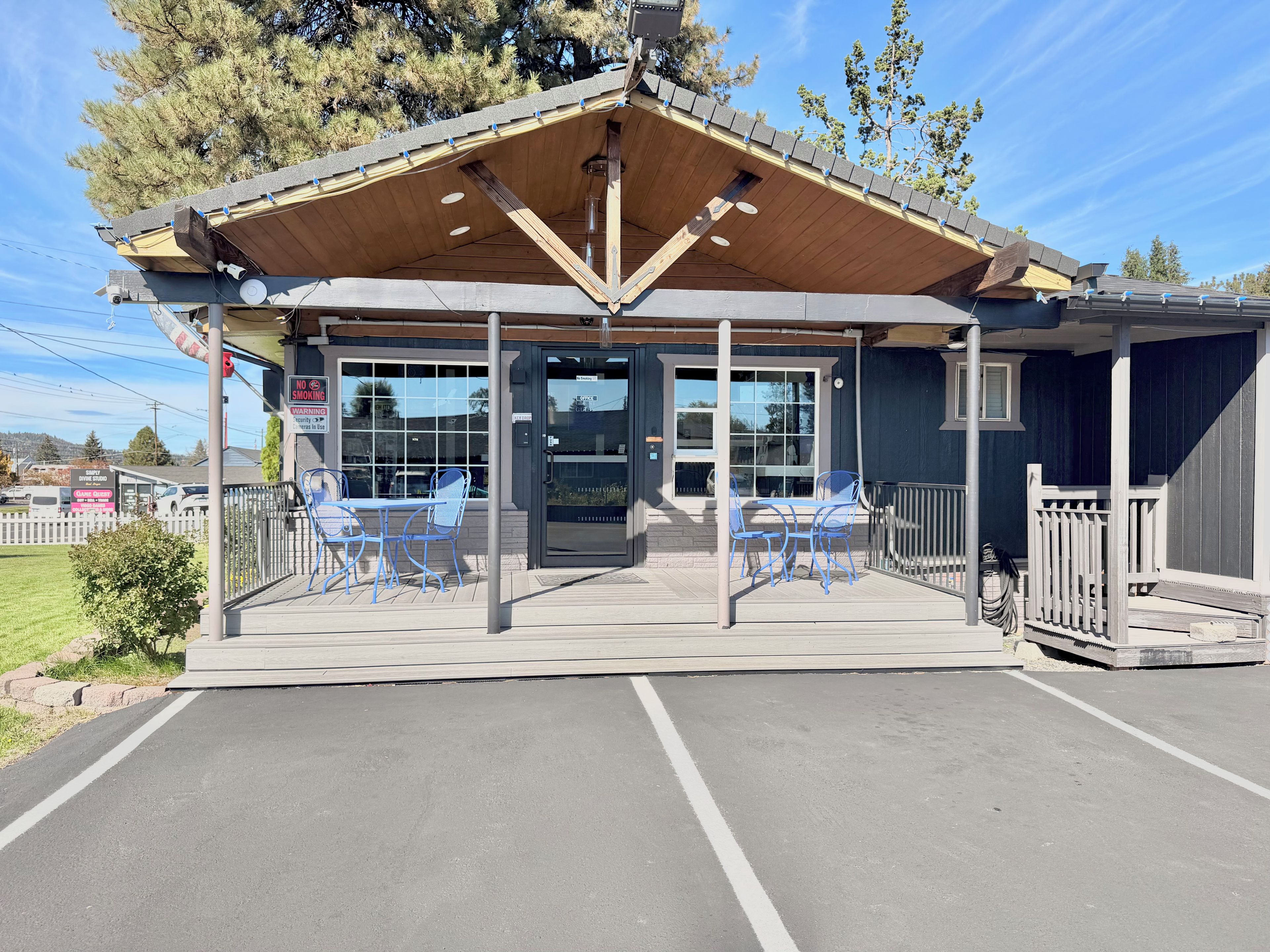 A covered outdoor seating area with tables and chairs, a glass door entrance, and a wooden roof structure.