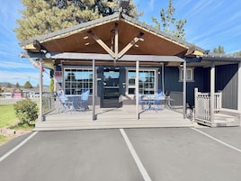 A covered outdoor seating area with tables and chairs, a glass door entrance, and a wooden roof structure.