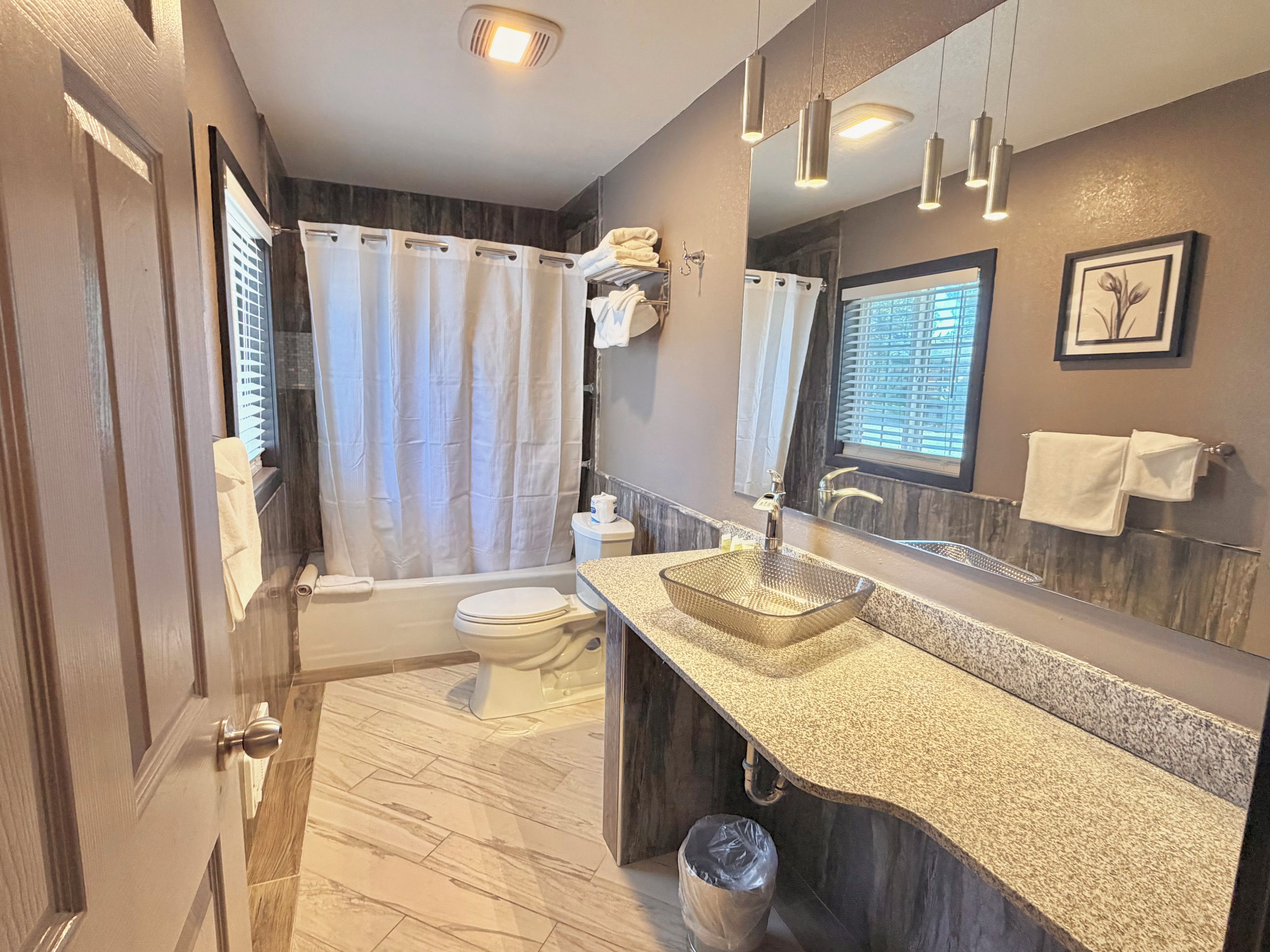 A modern bathroom with a glass sink, a bathtub, and a toilet.