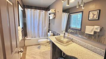 A modern bathroom with a glass sink, a bathtub, and a toilet.