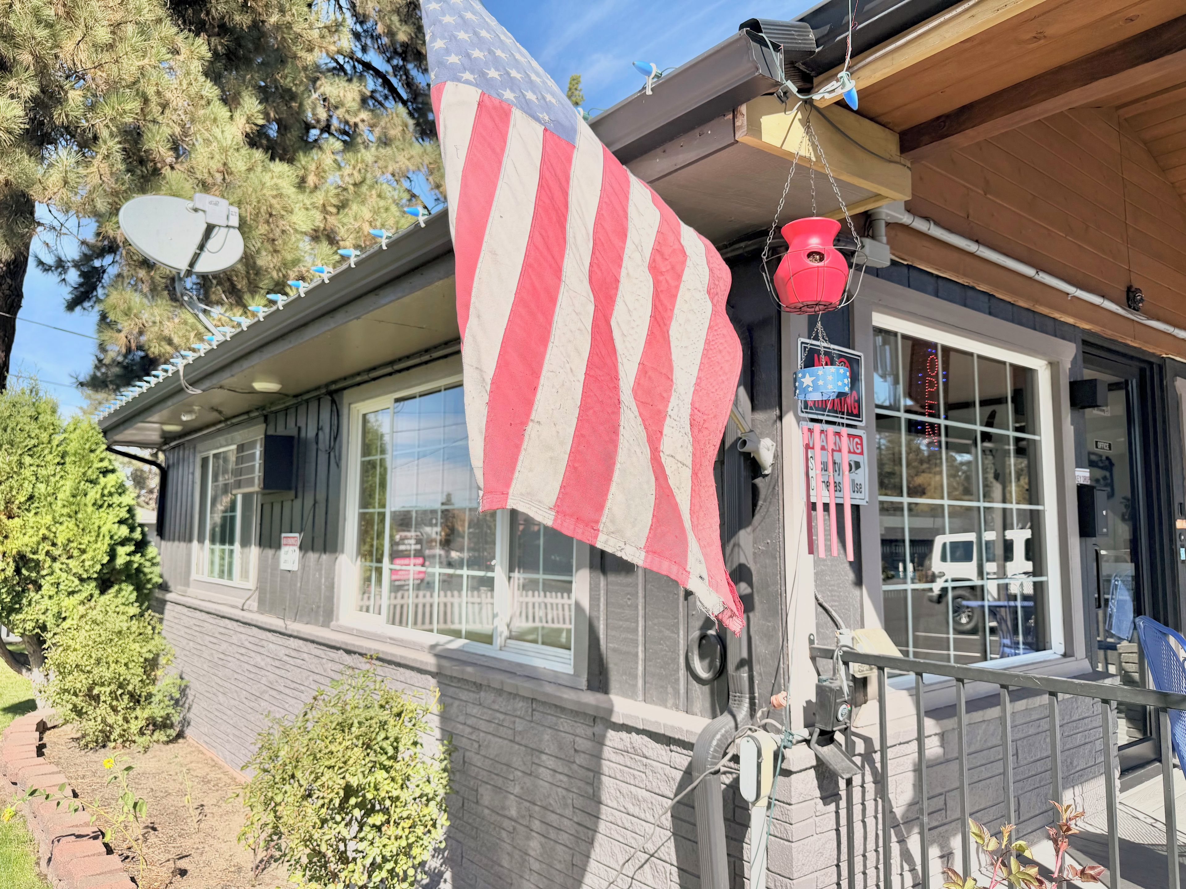 Une maison avec une antenne parabolique, un drapeau américain et un pot suspendu de couleur rouge.