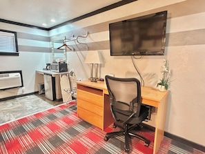 A hotel room with a desk, chair, TV, air conditioning unit, and a red and black checkered carpet. - Cascade Lodge Boutique (Bend)