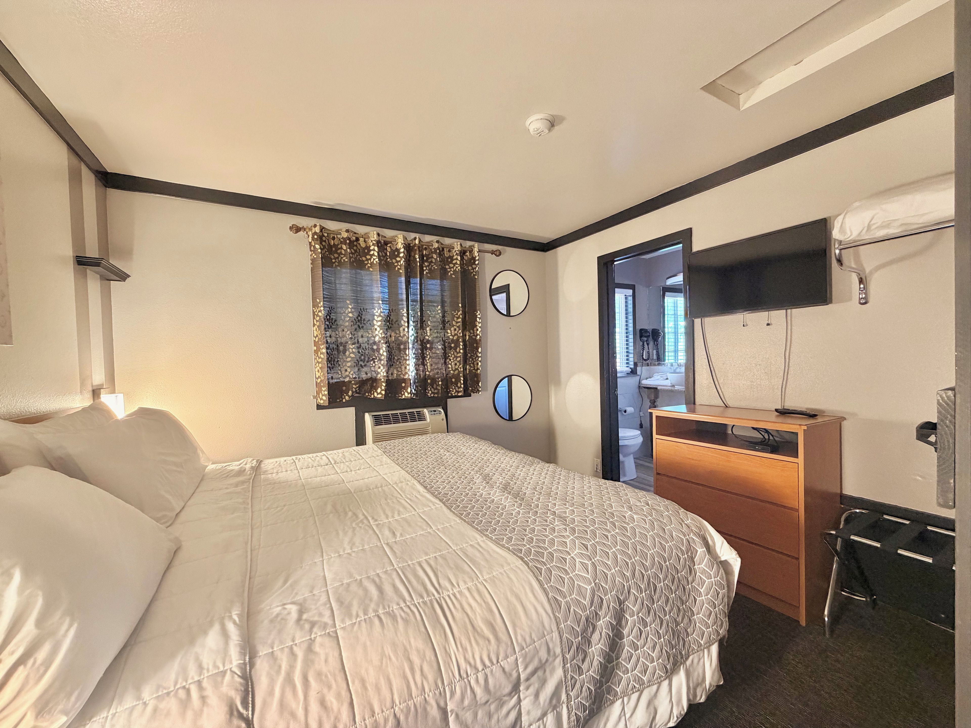 Een hotelkamer met een bed, een bureau, een spiegel, een televisie en een deur naar een badkamer.