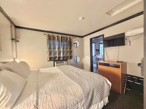 Een hotelkamer met een bed, een bureau, een spiegel, een televisie en een deur naar een badkamer.