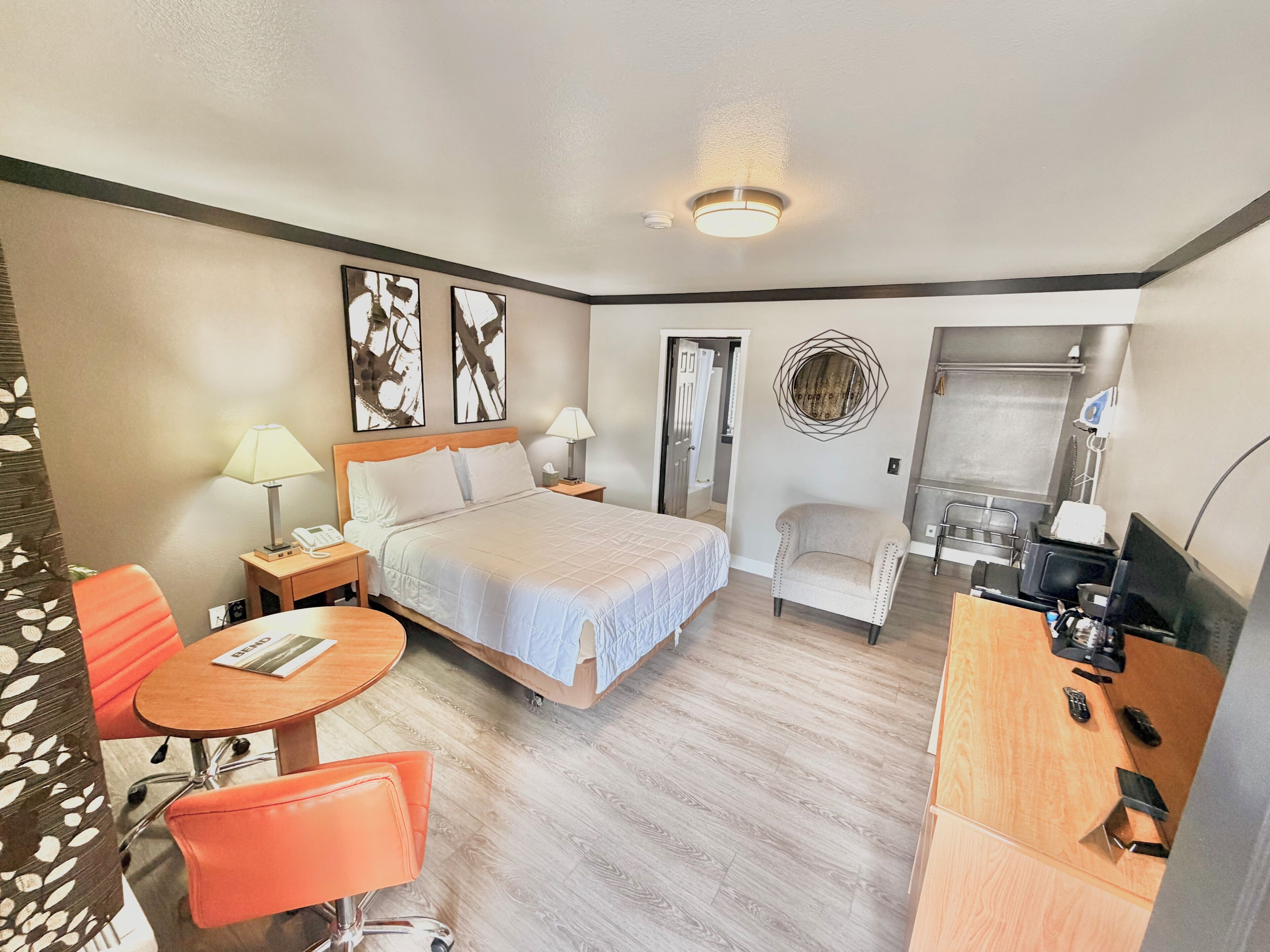 Une chambre d’hôtel comprenant un lit, des tables de chevet, un bureau, une chaise, un téléviseur et une salle de bain visible à travers une porte ouverte.