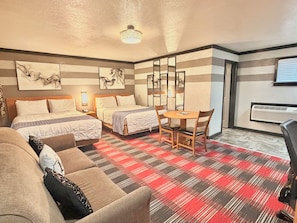Habitación de hotel con dos camas, una mesa de comedor con sillas, un sofá y un espejo grande.