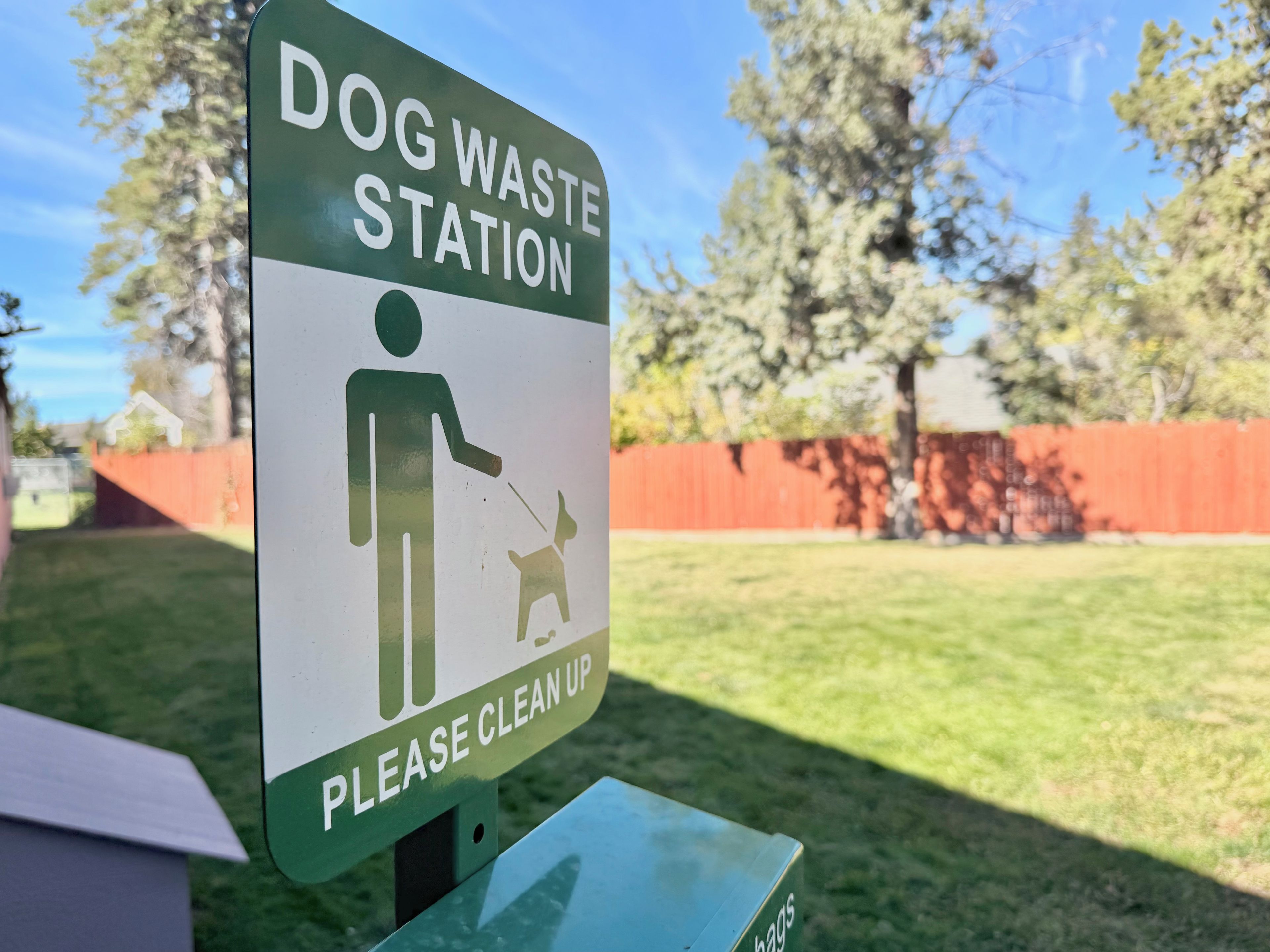 A sign indicating a dog waste station with a pictogram of a person and a dog, and a request to clean up.