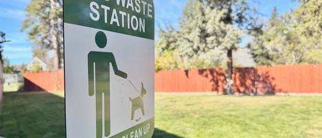 A sign indicating a dog waste station with a pictogram of a person and a dog, and a request to clean up.