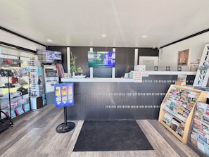 A reception desk with a TV screen, a pet fee sign, and a display of travel magazines. - Cascade Lodge Boutique (Bend)