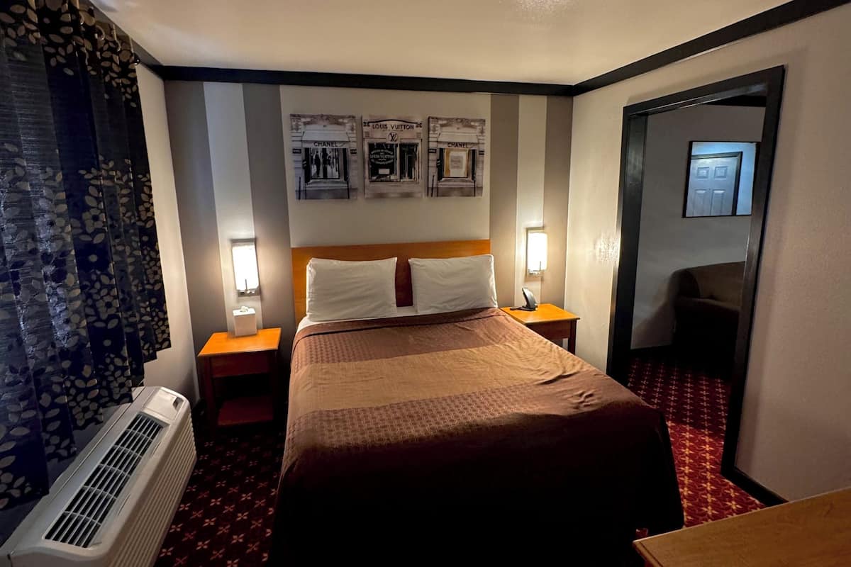 A hotel room with a bed, a heater, a mirror, and wall art.
