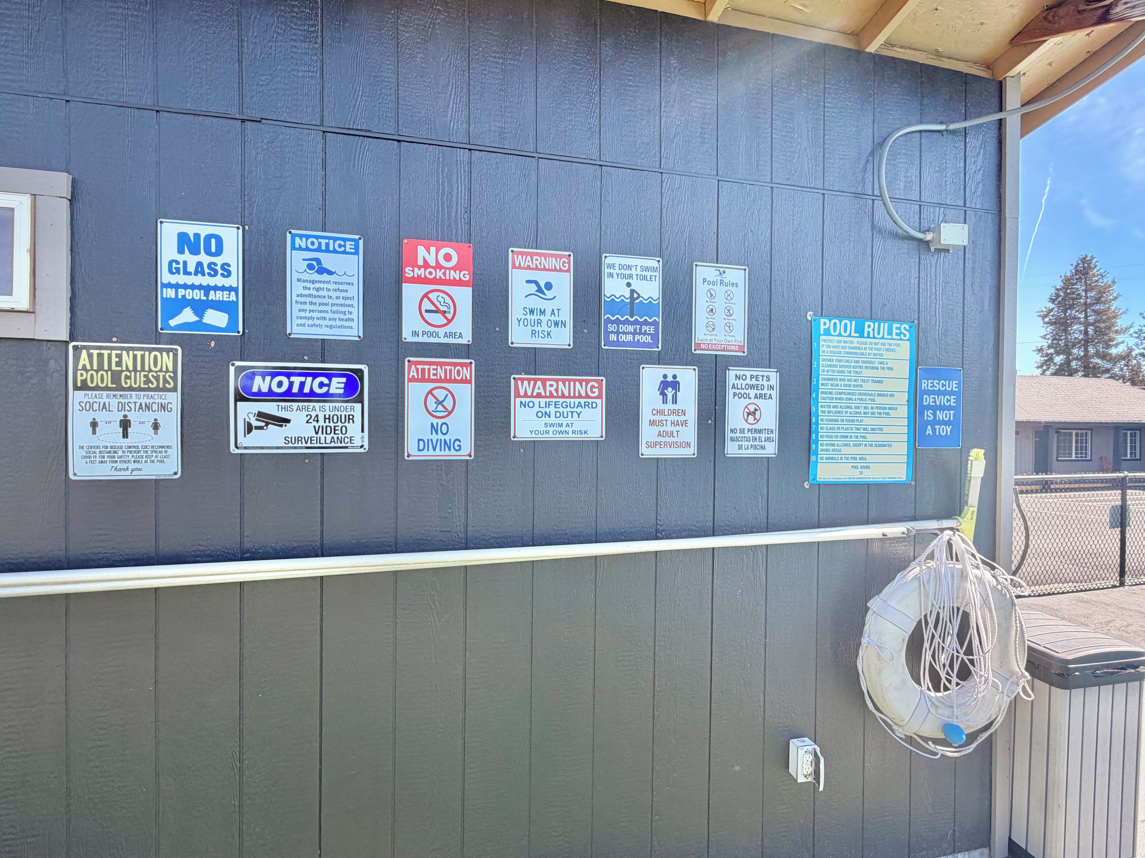 Un mur sur lequel sont affichés de nombreux panneaux indiquant les règles de sécurité et les consignes à respecter au bord de la piscine.