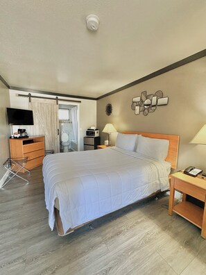 A hotel room with a large bed, a TV, a desk with a lamp, and a bathroom visible through a sliding door. - Cascade Lodge Boutique (Bend)