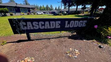 En træbænk med teksten "CASCADE LODGE", omgivet af en have med grus og blomster.