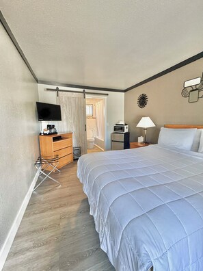 A hotel room with a bed, a desk with a computer, a television, and a bathroom visible through an open door. - Cascade Lodge Boutique (Bend)