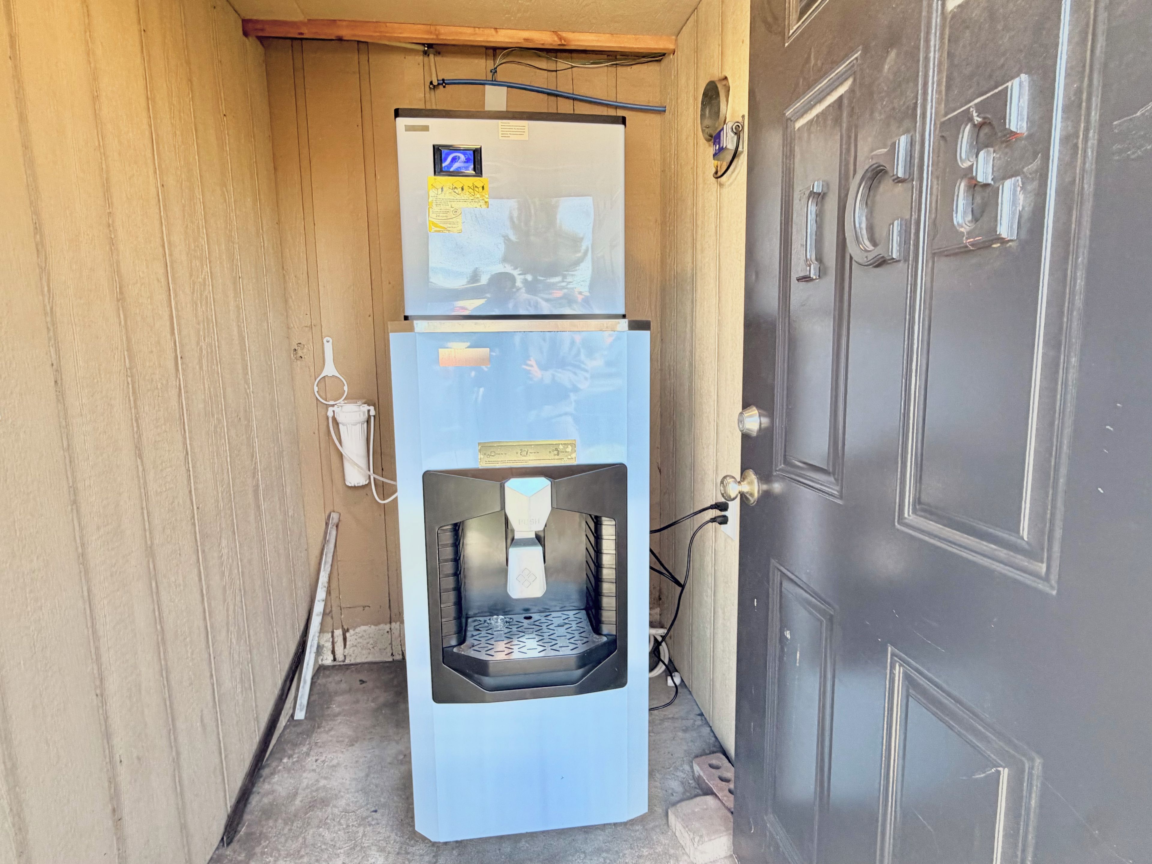 A compact room with a door, a water dispenser, and a small refrigerator.