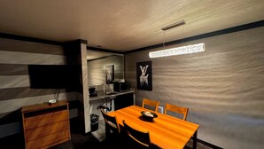 A compact room with a wooden dining table, two chairs, a small wooden cabinet, a flat-screen TV mounted on the wall, a built-in shelf with a microwave, and a wall-mounted light fixture. - Cascade Lodge Boutique (Bend)