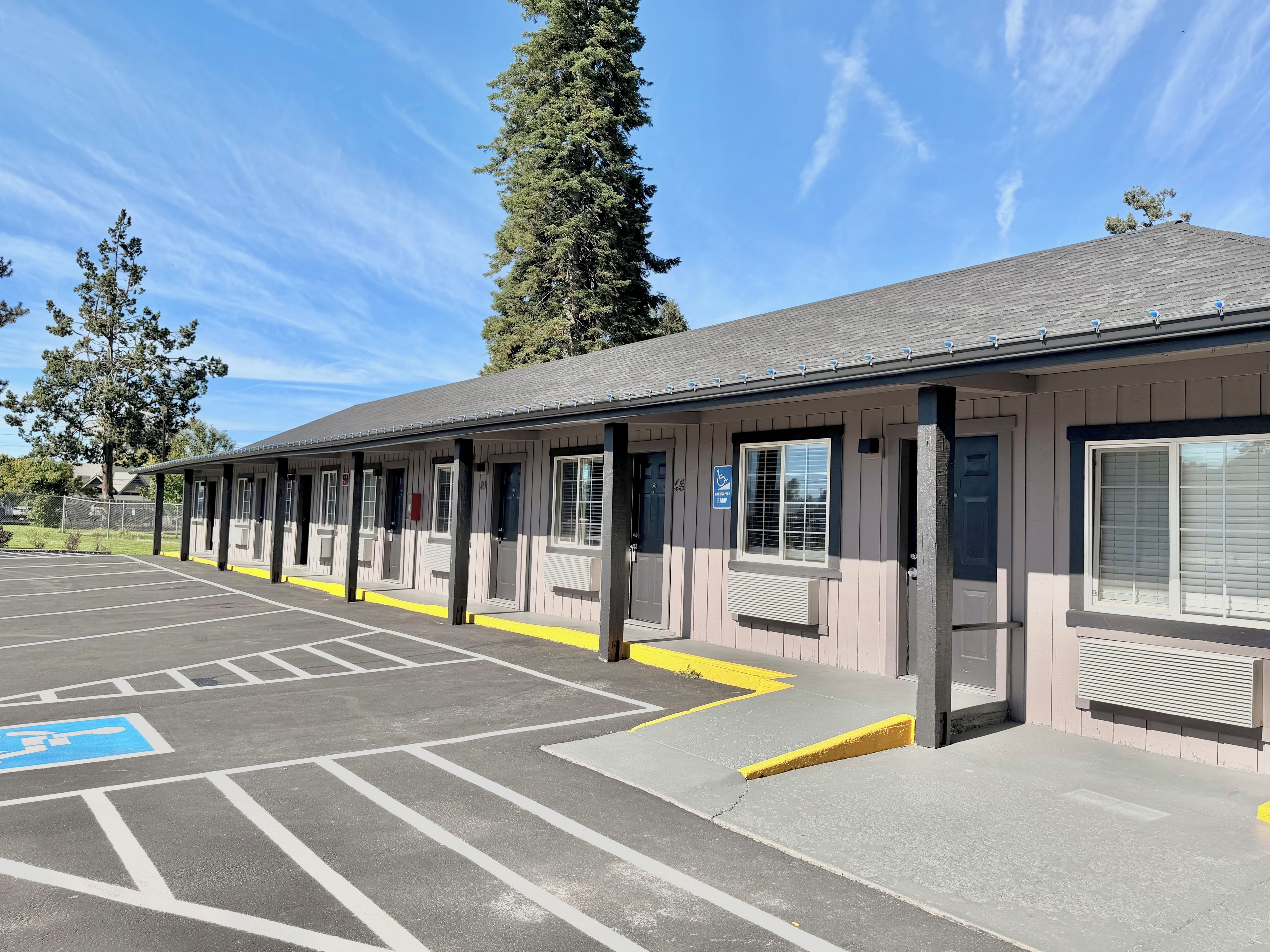 A building with a covered outdoor area, marked parking spaces, and a wheelchair-accessible ramp.