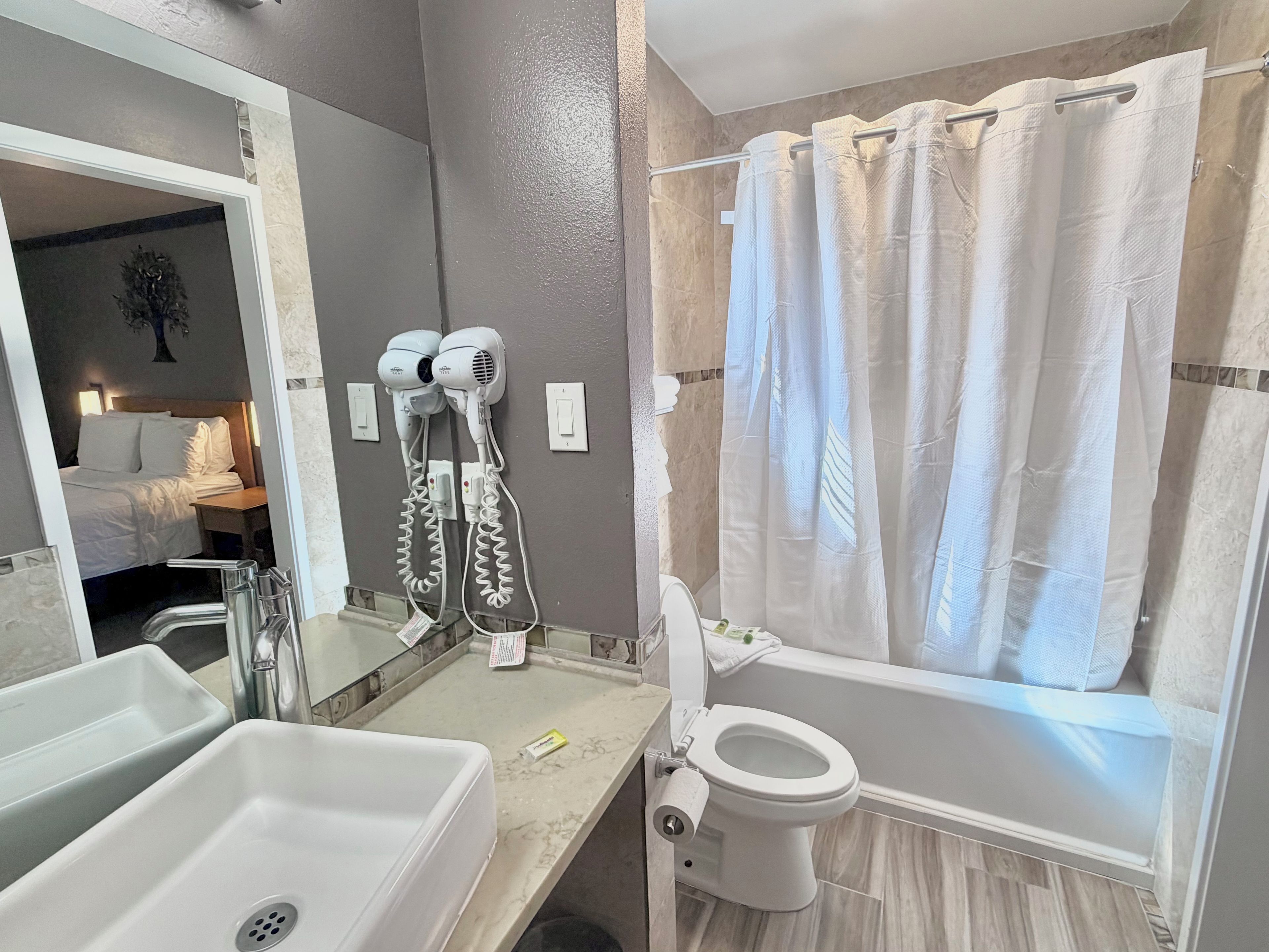 Un baño con bañera, inodoro y lavabo. Hay secadores de pelo montados en la pared.