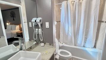 Un baño con bañera, inodoro y lavabo. Hay secadores de pelo montados en la pared.