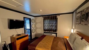 A hotel room with a bed, a TV mounted on the wall, a dresser, a window with curtains, and a wall-mounted air conditioner. - Cascade Lodge Boutique (Bend)